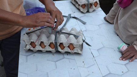 A vendor is tying eggs to a cardboard box. Eggs are inside the carton and tied together with plastic...
