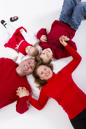 Girls and boys together as a family happily smiling to you on the floor hand to hand. 7 years old brother and 3 months sister and their happy parents.の写真素材