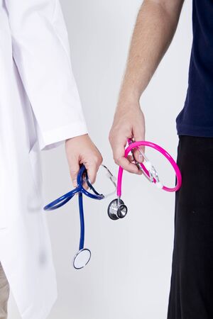Male and female doctors each holding stethoscope. Male blonde doctor has pink and female one holding dark blue stethoscope.の写真素材