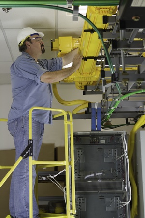 A telecommunication switch worker inspecting Fiberoptic cables in the fiberduct on a OSHA approved ladder platform.の写真素材