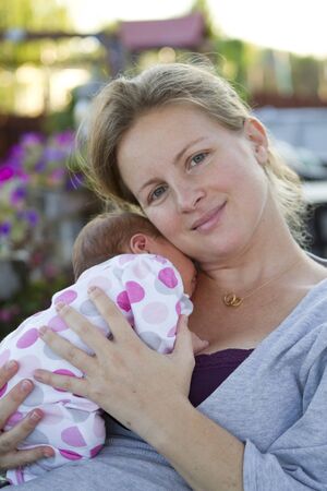 Tired mom holding her baby and relaxing outside after her baby turns week old.の写真素材