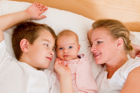 Mother and her kids in the bed, big brother and mother looking at  newborn swaddled newborn.の写真素材