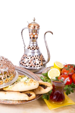 Made with cheese and seasoned ground beef Turkish pide garnished with lemon parsley and tomatoes on the vine. Served with tea and in copper plate.の写真素材