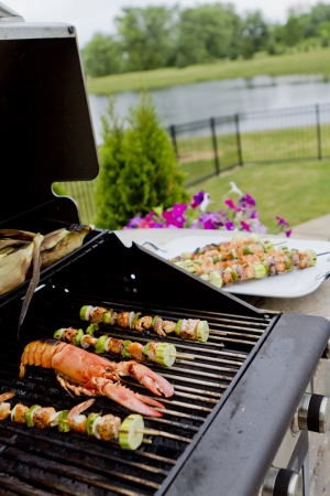 Mediterranean fish shish kebabs and lobsteron the BBQ almost ready. Hungry people waiting.の写真素材