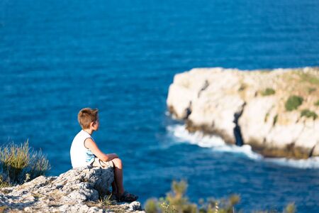 Young kid peacefully watching the waves of Black Sea. He is high sitting on the rocks.の写真素材