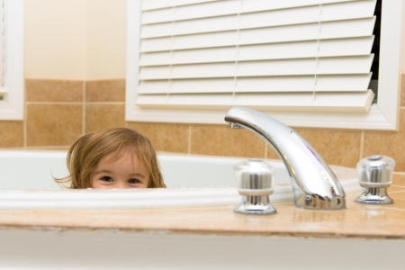 Toddler girl giving happy hiding look from the bathtub, perhaps she does not want to take a bathの写真素材
