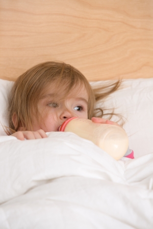 Cute toddler getting nutritious milk before goes to sleep under the blanket.の写真素材