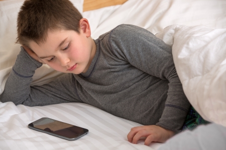 Eight years old kid watching shows on daddy's smart phone before he goes to sleep.の写真素材