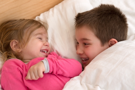 Siblings laughing at each other in the bed, happy cozy moments.の写真素材