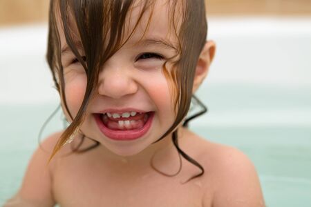 Squeezed eyed, teething toddler girl  giving a big laugh with wet hair の写真素材
