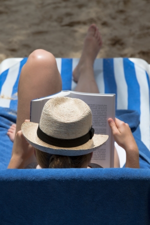 Lady in hat reading her book  on the beach reclinerの写真素材