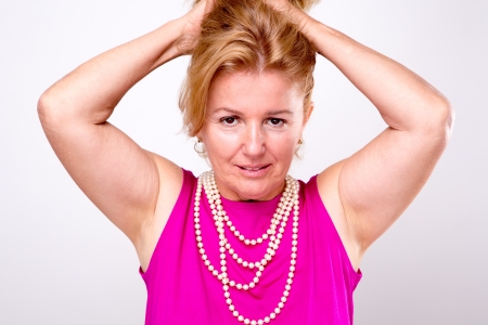 Mature Blonde Lady with Both Arms up holding her hair, she has pearl necklace and  pink shirtの写真素材