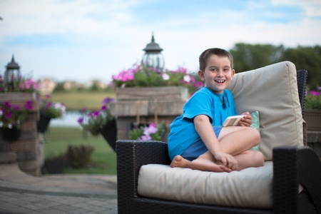 Young boy smiling at camera with a large genuine smile on the wicker seat at the patioの写真素材