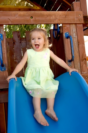 Two years old girl fulfilled on the blue slide that attached to the wooden playgroundの写真素材