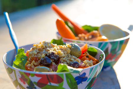 Healthy spinach salad made with tomatoes, carrots, green and black olives, and garnished with walnut, olive oil and lemon. Ready to eat under the early morning sunlight.の写真素材