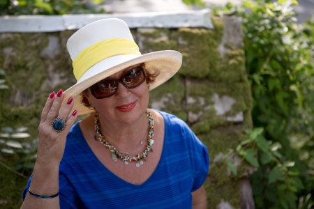 Senior lady with the hat and glasses infront of the greenery posing.の写真素材