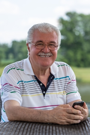 Grey hair senior gentleman looking trustfully with his glasses while holding his phone.の写真素材