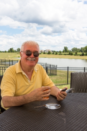 Senior Man posing with his smart phone  while drinking his Turkish tea at the patio by the pondの写真素材