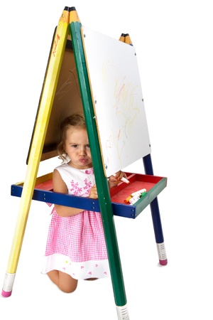 Tricks mischievous girl hiding in between whiteboard legs not happy to do homeworkの写真素材