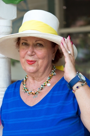 Beautiful chic senior woman in a wide-brimmed straw sunhat and fashionable jewellery looking at the camera with a lovely smileの写真素材