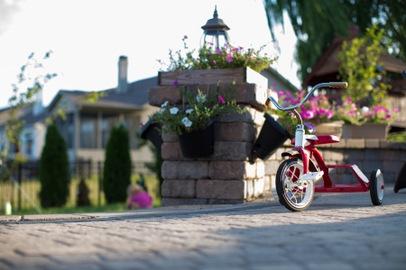 Childs red tricycle parked on a paved patio overlooking a garden in a shaft of sunlightの写真素材