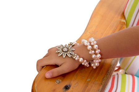 Young girl wearing a pearl and foral bracelet entwined several times around her wrist, close up view of her hand resting on the arm of a wooden chairの写真素材