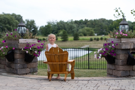Little blonde smiling from a garden chair  back to the camera overlooking open countryside and a small lake on a brick patioの写真素材