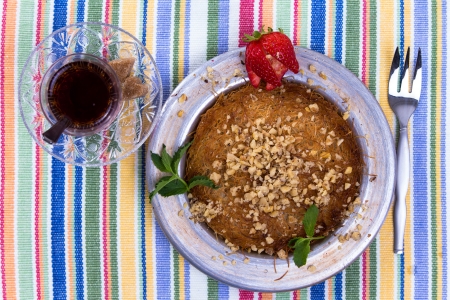 Turkish dessert kunefe on a picnic cloth with mint leaves and sliced strawberry along with Turkish tea and forkの写真素材