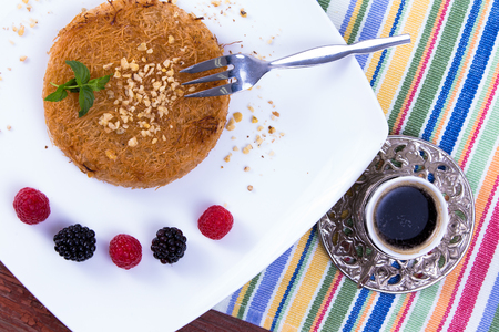 Turkish dessert kunefe  served with Turkish Coffee on a white plate with mint leaves along red and black berries on a picnic tableの写真素材