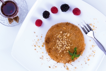 Turkish dessert kunefe  served on a white plate with mint leaves and sliced strawberry along red and black berriesの写真素材