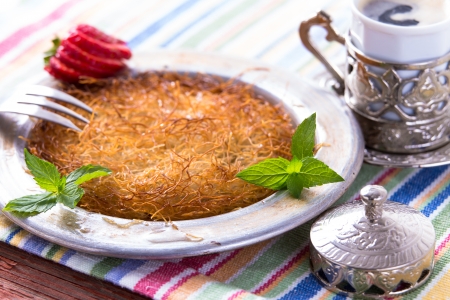 Turkish dessert kunefe  served in classical aluminum plate on a picnic table with mints and sliced strawberry along with Turkish cofffeeの写真素材