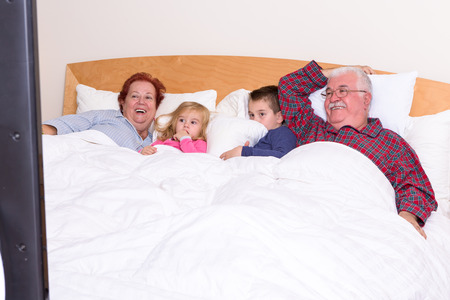 Grandparents watching TV in the bed with their grand kids, they look excited, perhaps its an adventure movieの写真素材