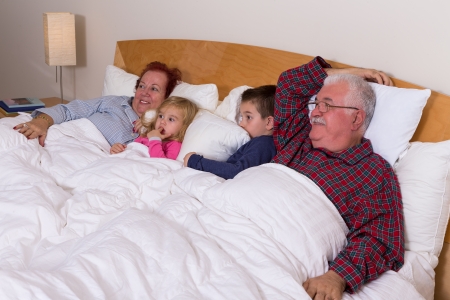 Grandparents watching TV in the bed with their grand kids, they look excited, perhaps its an adventure movieの写真素材