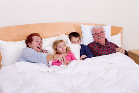 Grandparents watching TV in the bed with their grand kids, they look excited, perhaps its an adventure movieの写真素材