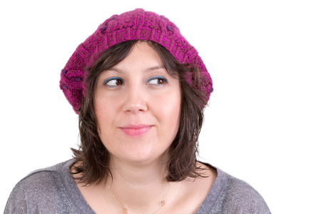 Thoughtful woman wearing a knitted purple winter cap smiling in anticipation of being able to realise her dreams, looking off with her eyes to the side and smiling, isolated on whiteの写真素材