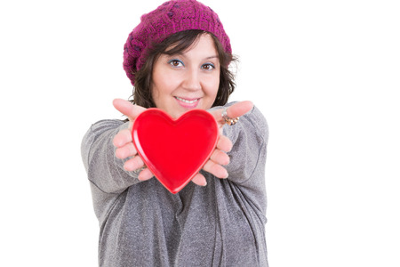 Happy woman holding out a red valentines heart for her sweetheart in her extended hands with a tender smile isolated on whiteの写真素材