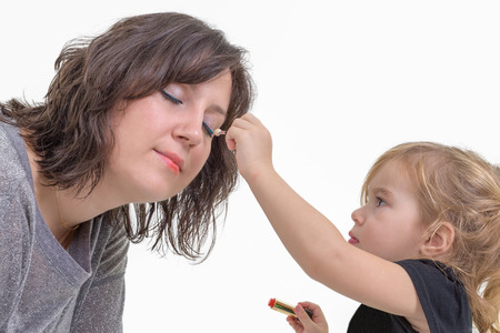 Adorable litte blond girl applying makeup to her mother putting eyeshadow on her eyes, isolated on whiteの写真素材