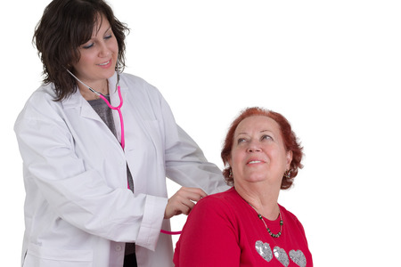 Female doctor examining an elderly woman patient with a stethoscope in her clinic as the two women smile at each other, isolated on whiteの写真素材
