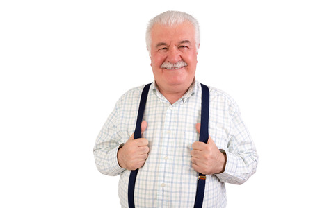 Confident senior grey-haired man with a moustache and beaming friendly smile holding his suspenders or braces, upper body isolated on whiteの写真素材