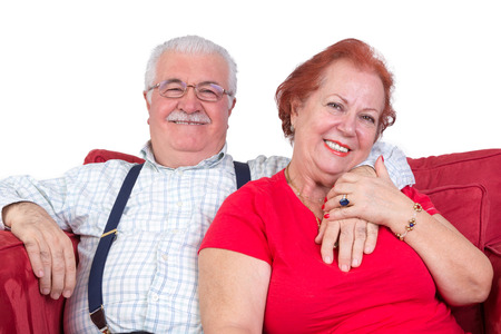 Good natured senior couple relaxing together in a close embrace looking at the camera with charming friendly smilesの写真素材
