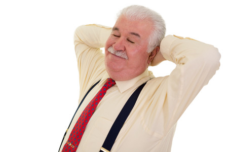 Contented grey-haired senior man with a moustache wearing suspenders relaxing with his hands behind his head and his eyes closed with a smile of satisfaction, on whiteの写真素材