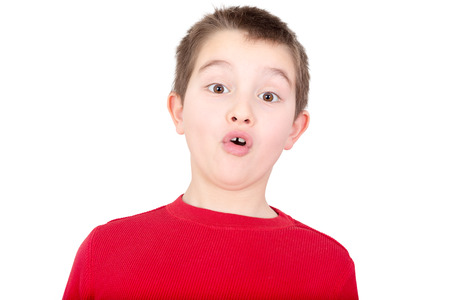 Young boy reacting with a look of amazement and awe as he stares wide eyed at the camera with his mouth forming on oh, isolated on whiteの写真素材
