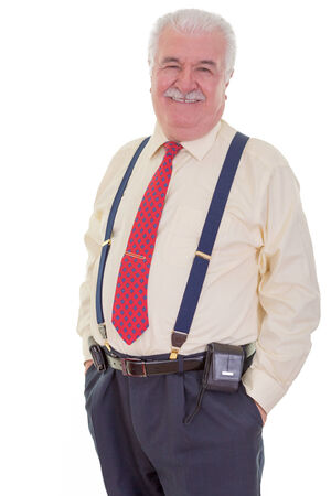 Confident portly senior gentleman with a moustache wearing braces and a tie standing in a relaxed pose with his hands in his pocket smiling at the cameraの写真素材