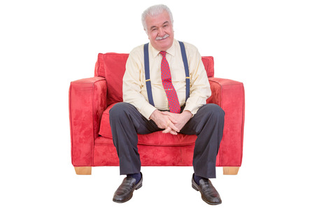 Studio portrait over white of a senior white haired man relaxing in a comfortable red armchair.の写真素材
