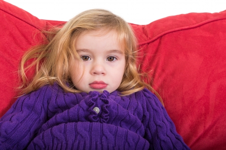 Cute solemn beautiful young girl staring at the camera with a calm expression as she relaxes on a comfortable red cushion in her colourful purple sweaterの写真素材