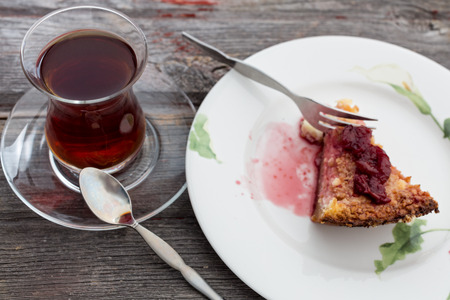 Slice of delicious cheesecake topped with a berry compote and served with a tall glass of freshly brewed Turkish tea on an old wooden tableの写真素材
