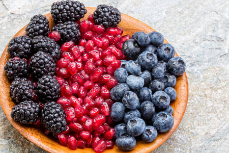 Wooden bowl of fresh blueberries, blackberries and pomegranate seeds arranged in colourful rows,...