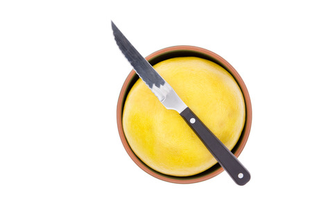 Kitchen knife on a ripe yellow grapefruit or pomelo fitted tightly into a small bowl ready to be cut and prepared for breakfast, isolated on white with copypace, overhead viewの写真素材