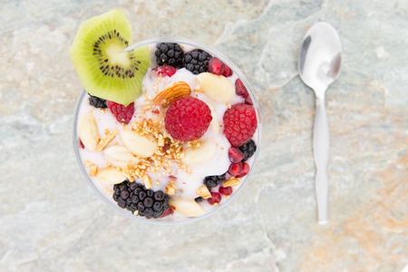 Overhead view of a frozen parfait dessert topped with fresh raspberries, blackberries and almond nuts and garnished with a slice of tropical kiwifruitの写真素材