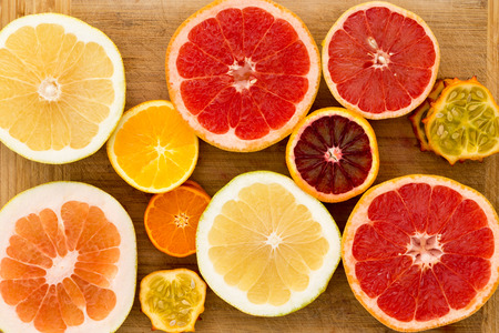 Colorful festive assortment of halved citrus fruit arranged on a wooden board with a variety of grapefruit, orange, pomelo and kiwano or horned melon viewed from aboveの写真素材